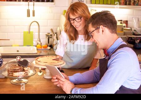 Shot of happy small business owner woman and young waiter standing at counter and using digital tablet while working together. Small business. Stock Photo
