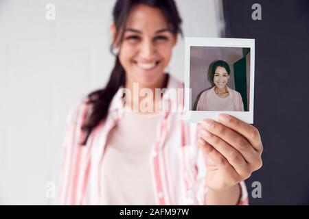 Portrait Of Female Photographer On Photo Shoot Holding Up Instant Polaroid Print In Studio Stock Photo