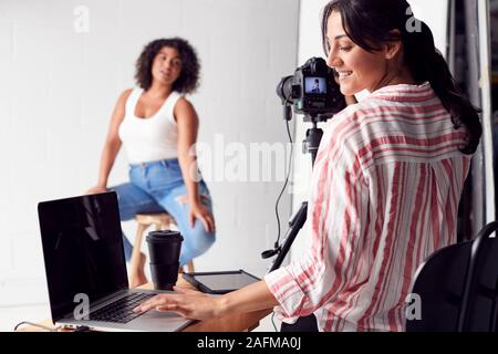 Female Photographer In Digital Studio Shooting Images On Camera Tethered To Laptop Computer Stock Photo
