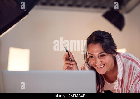 Female Photographer Editing Images From Photo Shoot On Laptop In Studio Stock Photo