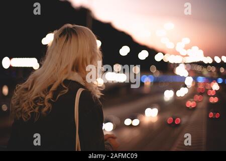 Rear view of young woman looking at road standing on bridge in city Stock Photo