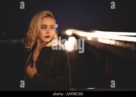 Portrait of young woman standing against illuminated bridge in city