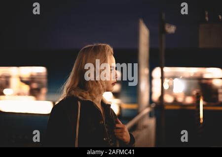 Young woman standing at subway station by moving train at night Stock Photo