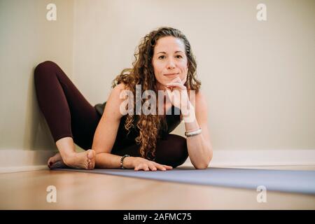 fit woman with curly hair relaxes on yoga mat in corner of studio Stock Photo