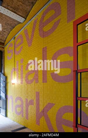 Graphic writing on yellow brick wall. Seven Dials Market, London, United Kingdom. Architect: Stiff + Trevillion Architects, 2019. Stock Photo
