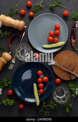 Frugal low calorie dinner for two flat lay. Half empty plates with tomatoes and cucumbers and empty glasses on black background overhead view Stock Photo