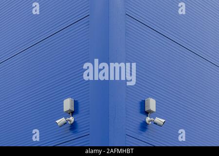 two small white security cameras on blue steel building corner. Stock Photo