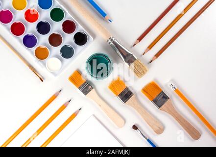 Education art concept. Set of watercolor paints, different sizes brushes, blank canvas and various pencils on light background. View from above. Drawi Stock Photo