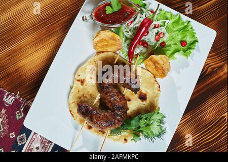 Healthy barbecued lean cubed pork kebabs served with a corn tortilla and fresh lettuce and tomato salad, close up view on a dark background Stock Photo