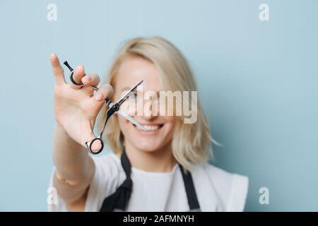 Stylish blonde female hairdresser holding open scissors in outstreched hand Stock Photo