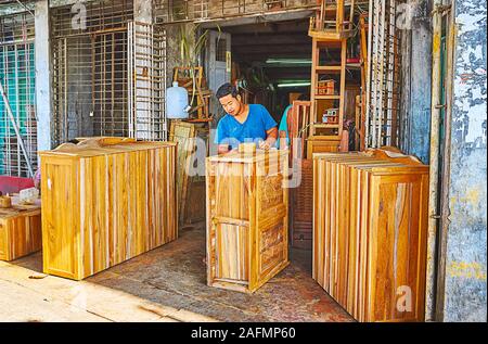 YANGON, MYANMAR - FEBRUARY 17, 2018: The young carpenter works in Chinatown street at the entrance to the workshop, on February 17 in Yangon Stock Photo