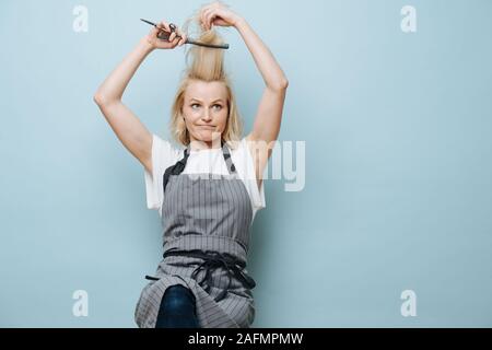 Playful blonde lady hairdresser pulling her bang up, making funny face Stock Photo