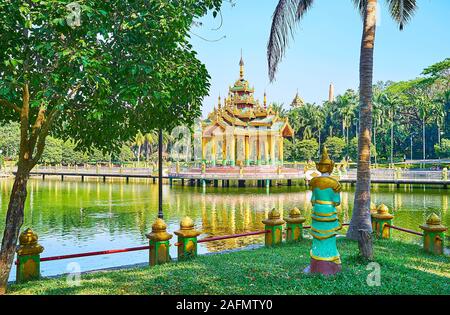 The view on small Buddhist shrine on the lake throught the lush trees on the bank in Theingottara park, Yangon, Myanmar Stock Photo