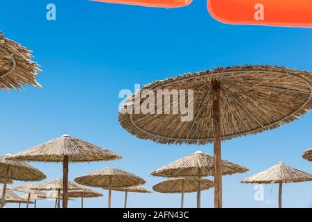 Wicker and textile orange umbrellas on the beach. Blue sky. Stock Photo