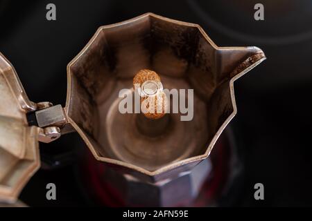 Process of brewing fresh coffee in a mocha pot on a red hotplate: Coffee is rising and sprinkling into the pot while forming bubbles, close-up Stock Photo