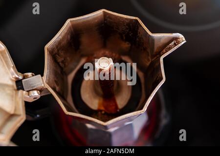Process of brewing fresh coffee in a mocha pot on a red hotplate: Coffee is rising and flowing into the pot, close-up, selective focus, horizontal Stock Photo