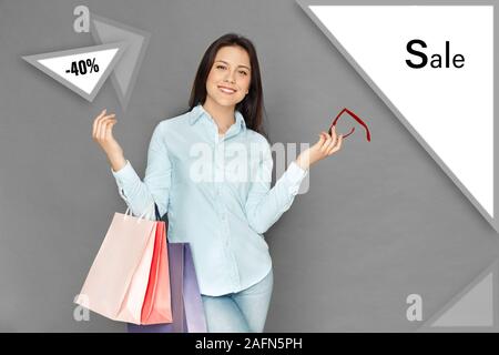 Freestyle. Young woman standing isolated on grey with shopping bags holding sunglasses joyful Stock Photo