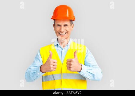 Construction. Mature man in hardhat and uniform standing isolated on white showing thumbs up laughing playful Stock Photo