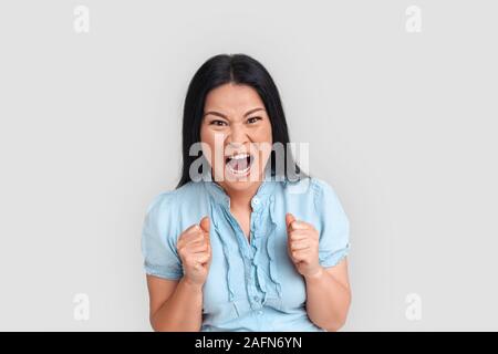 Freestyle. Asian woman standing isolated on white hands in fists shouting to camera angry Stock Photo