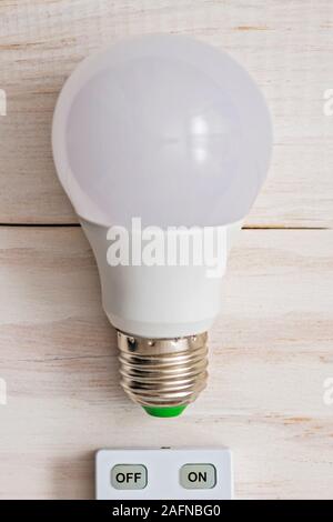 LED light bulb and remote control with buttons on and off on a white wooden background. Stock Photo