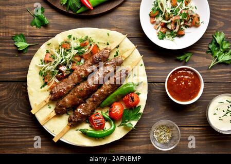 Tasty turkish Adana Kebab with fresh vegetables on flatbread over wooden background. Top view, flat lay Stock Photo