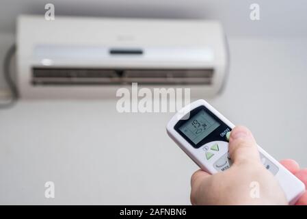 Hand with remote control directed on the conditioner on the wall. Air conditioner with remote controller. Stock Photo