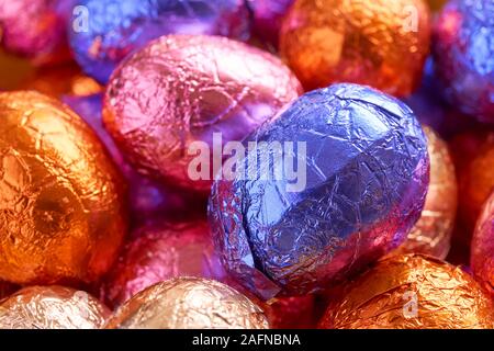 Many chocolate easter eggs wrapped in blue, purple, orange, pink and golden foil wrap Stock Photo