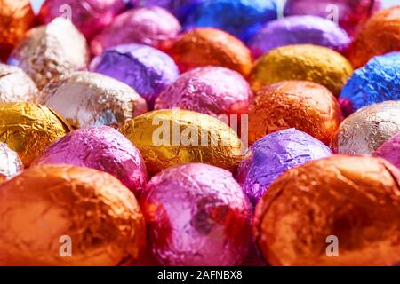 Many chocolate easter eggs wrapped in blue, purple, orange, pink and golden foil wrap Stock Photo
