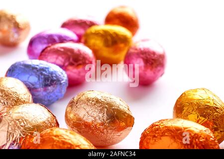 Many chocolate easter eggs wrapped in blue, purple, orange, pink and golden foil on a white background Stock Photo