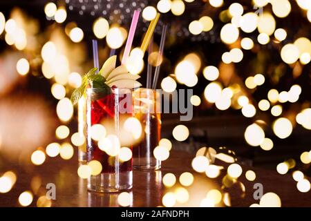 Cherry bomb, screwdriver and cuba libre cocktails in a tall glasses on the dark background. Shallow DOF and dark red tone with festive bokeh lights Stock Photo