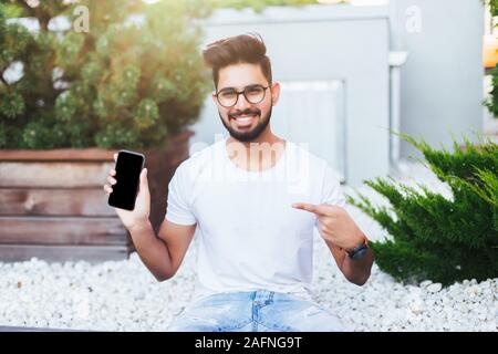 Indian man sitting on the bench pointed on the phone in the street Stock Photo