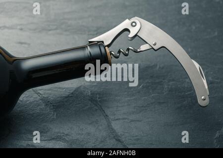 Stainless  wine corkscrew in a cork of wine bottle neck on a black rocky slate background Stock Photo