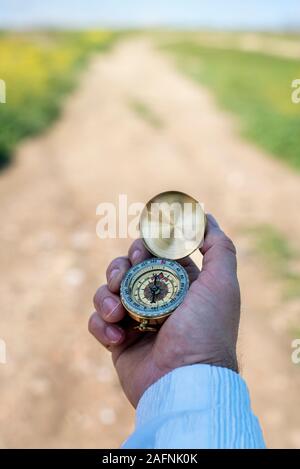 A man's hand holding a compass and an unfocused road in the background. Stock Photo
