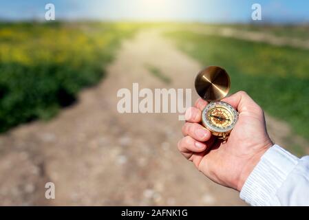 A man's hand holding a compass and an unfocused road in the background. Stock Photo