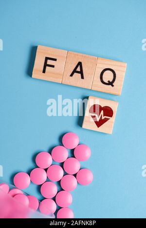 The concept of basic, general questions on medicines, pills for the heart. Pink tablets next to wooden square and letters - FAQ. Close up. Stock Photo