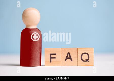 Abstract doctor with a medicine and an inscription: answers to popular questions - FAQ. A wooden figurine with cubes on a blue phone. Close up. Stock Photo