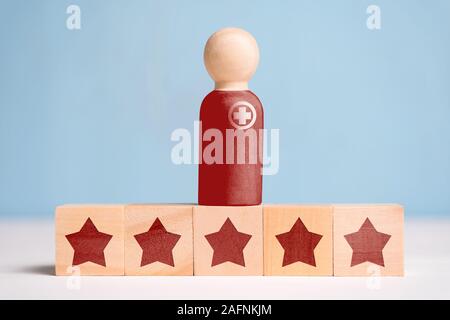 The concept of the abstract doctor and the indicator of his rating is 5 stars. A wooden figurine on cubes on a blue background. Close up. Stock Photo