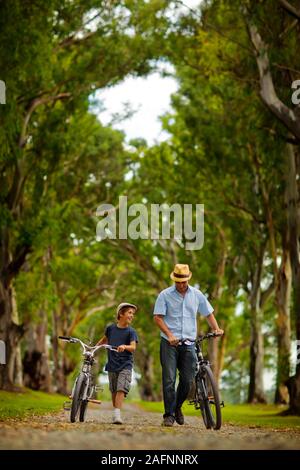 Father and son walking and pushing their bicycles. Stock Photo