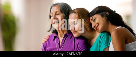 Three women leaning in to each other while sitting side by side on a patio. Stock Photo