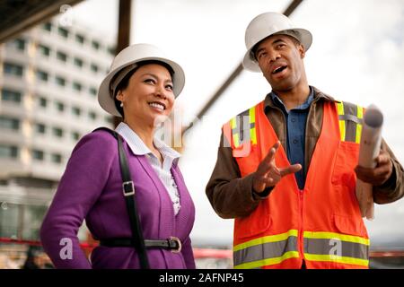 Two smiling engineers discussing plans on a construction site. Stock Photo