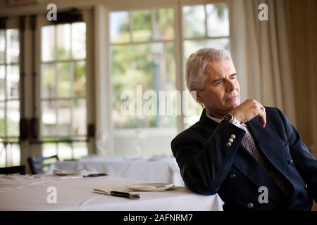 Businessman sits in restaurant looking into space in thought. Stock Photo