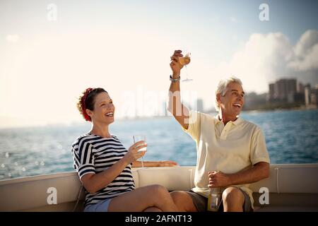 Mature couple toasting with glasses of wine as they sit on boat in harbour. Stock Photo