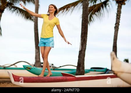 Mid adult woman balances while walking over kayak on the beach. Stock Photo