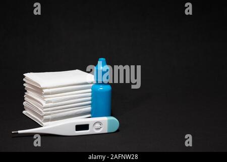 White paper tissues and white thermometer with blue nose drops on dark back background. Stock Photo