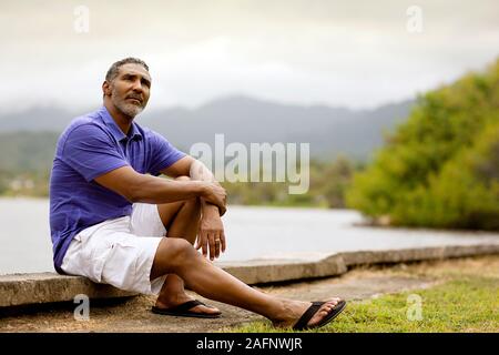 Mature man thoughtfully sitting on the curb by the beach. Stock Photo