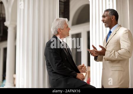 Two adult businessmen having a discussion on a portico. Stock Photo