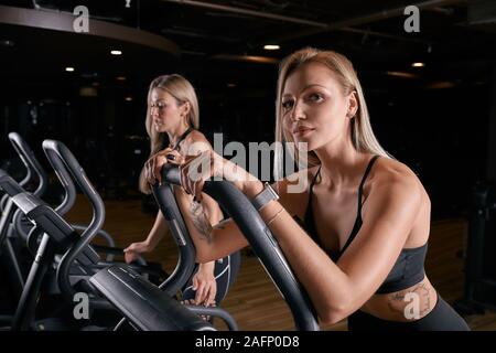 Two attractive sporty women riding exercise bikes during cycling training in gym. Stock Photo