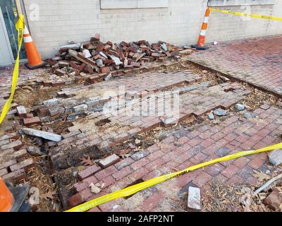 damaged red bricks on sidewalk with yellow caution tape and orange cones Stock Photo