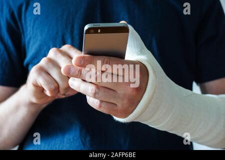 Man with plaster cast on broken hand, broken thumb,broken wrist using smartphone Stock Photo