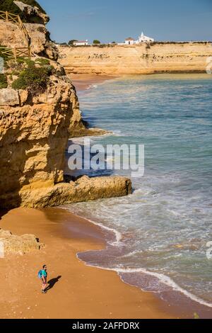 Walker on beach with Nossa Senhora da Rocha church in distance, Alporchinhas, Algarve, Portugal Stock Photo